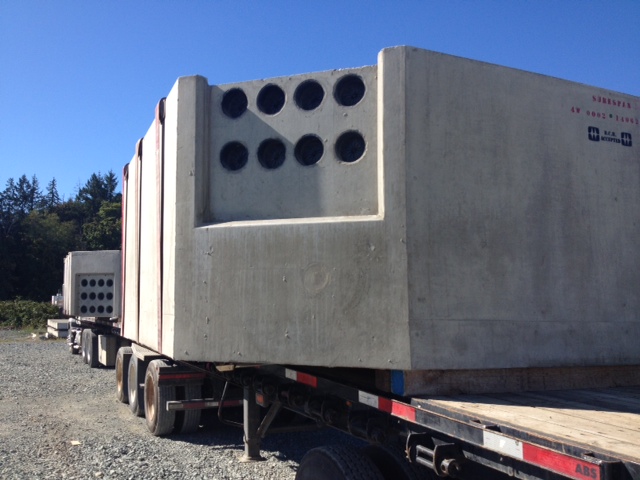 A front view of a transformer vault with 8 holes in the front. Is is a sunny day as a shadow is cast on the vault in front of a blue sky.