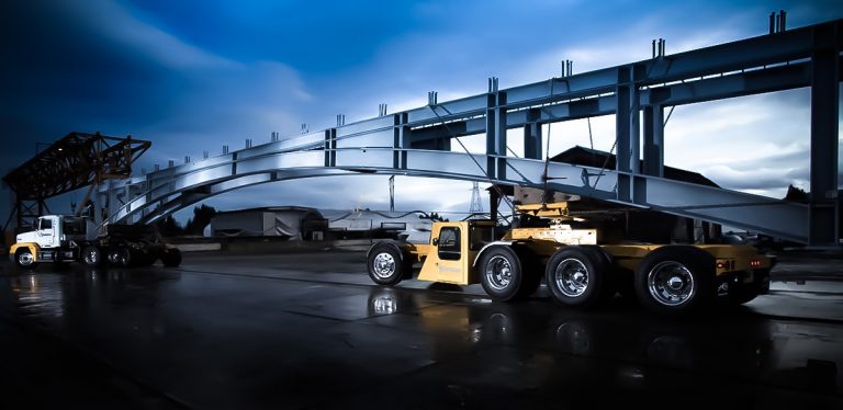 A side profile of the trucks that brought in the steel beams. There is a blue sky in the background with some clouds.