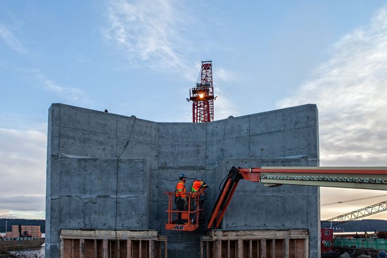 A piece of precast concrete can be seen in view. There is a man being transported by the Arctic Tuk as he is sheltered behind the concrete. It is a relatively clear day.