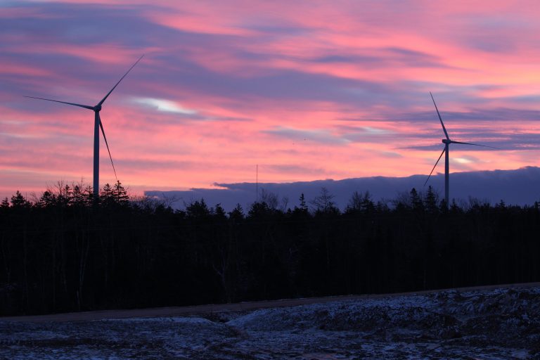 A bright pink and purple sunset can be seen cast over the installed turbines, bringing in the silhouettes of the trees to the front that highlights the beauty of the Nova Scotian landscape.