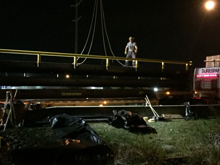 portable bridge rental for Highway 7 underway with workers in the background on a lit construction site.