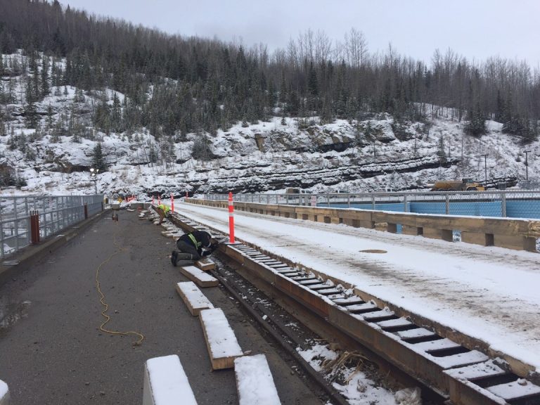 View on the bridge. There is a man working on the welding of the joints with mountains and trees in the background.