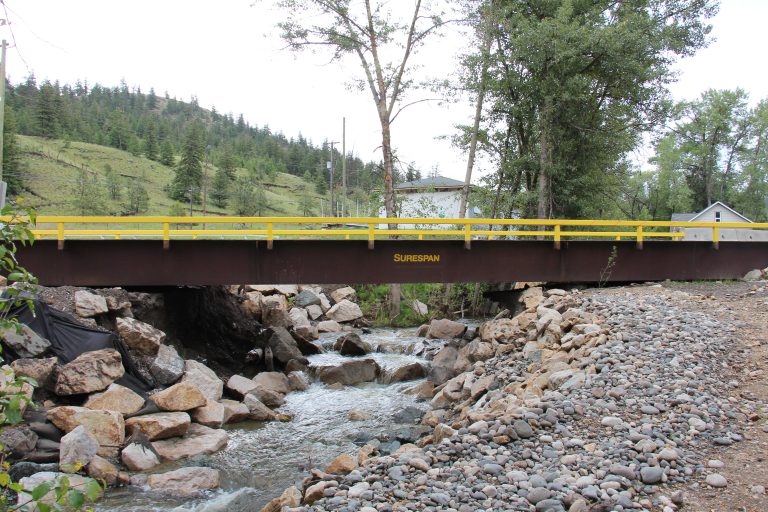 an angle of the surespan bridge rental with mountains and trees in the background. Rocks and dirt can be seen in the foreground.