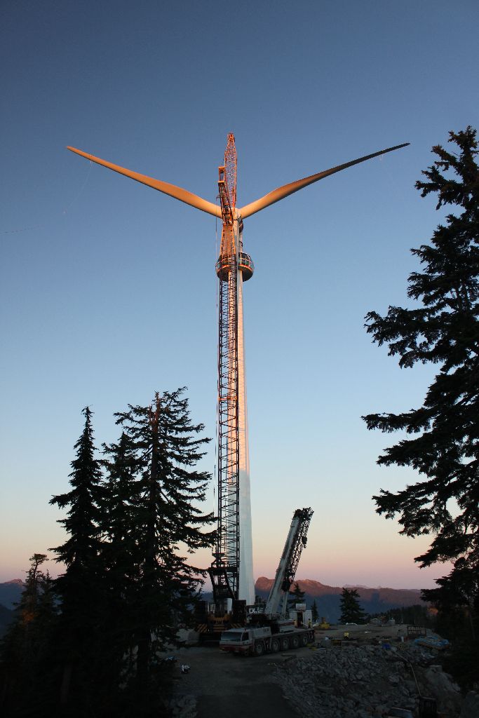 Side view of the completed turbine. There are some trees in the foreground over a dusky blue sky.